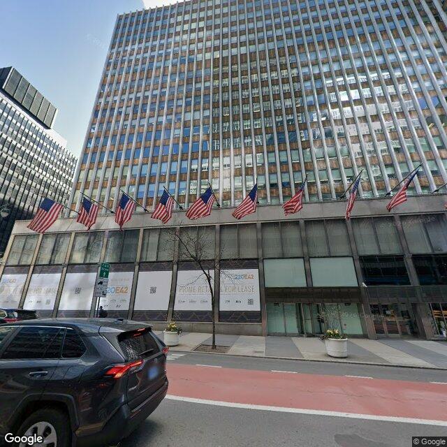 235 East 42nd Street, the former Pfizer headquarters, with its International Style curtain wall and a row of American flags. Street-level hoarding reads 220 E42 and PRIME RETAIL FOR LEASE, marking the active office-to-residential conversion.